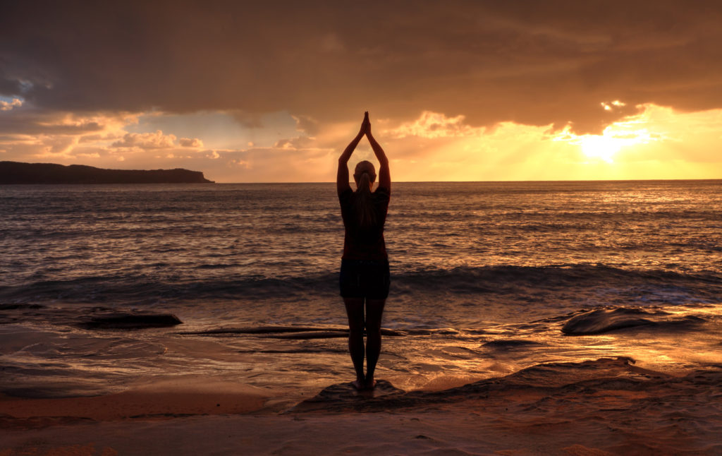 Female relaxing at sunrise, performing tadasana - mountain pose by the sea at sunrise