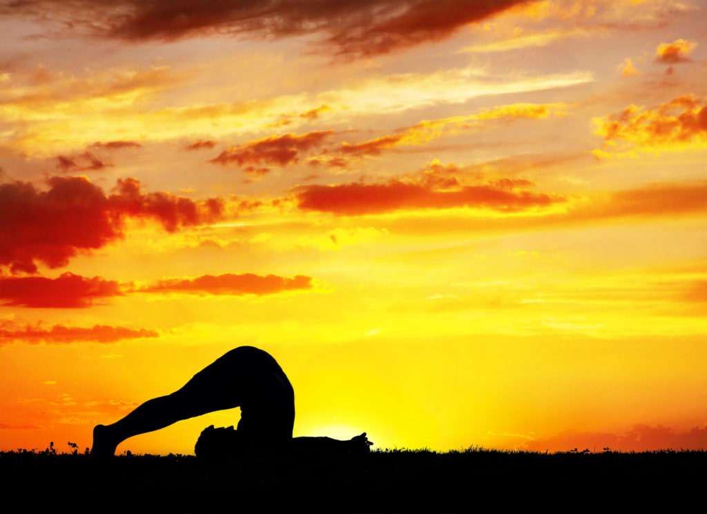 Yoga Halasana plough inverse pose by Man in silhouette with orange sunset sky background. Free space for text