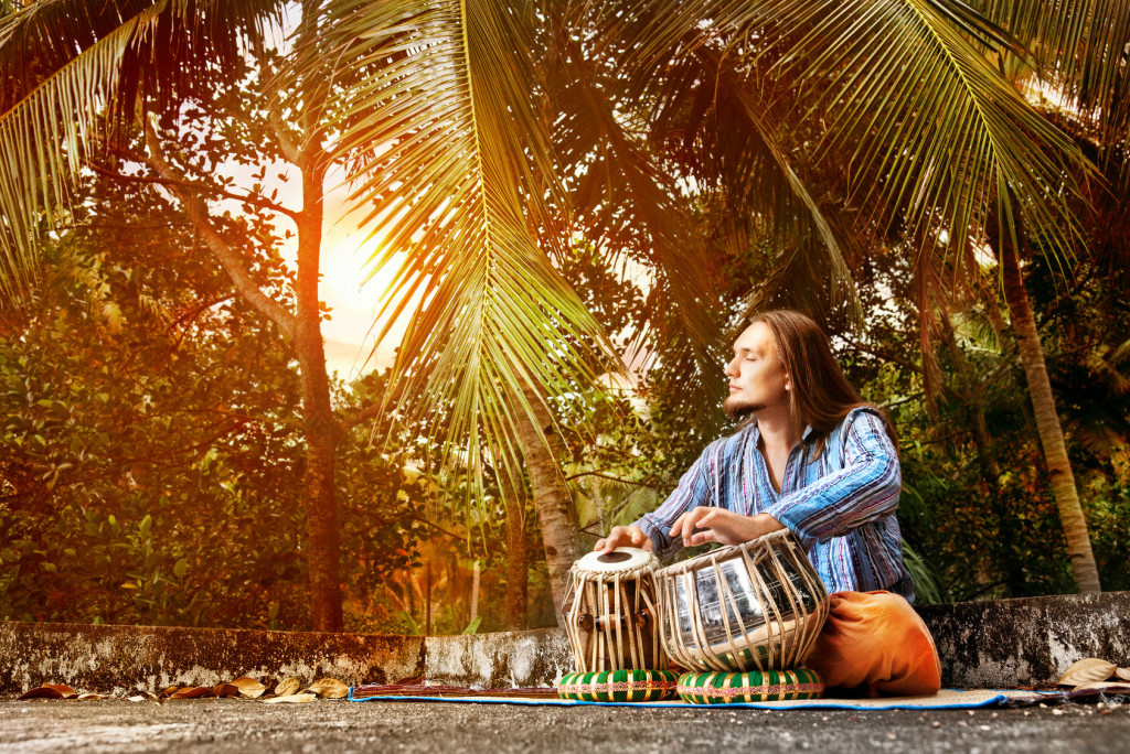 Man playing on traditional Indian tabla drums at sunset tropic background