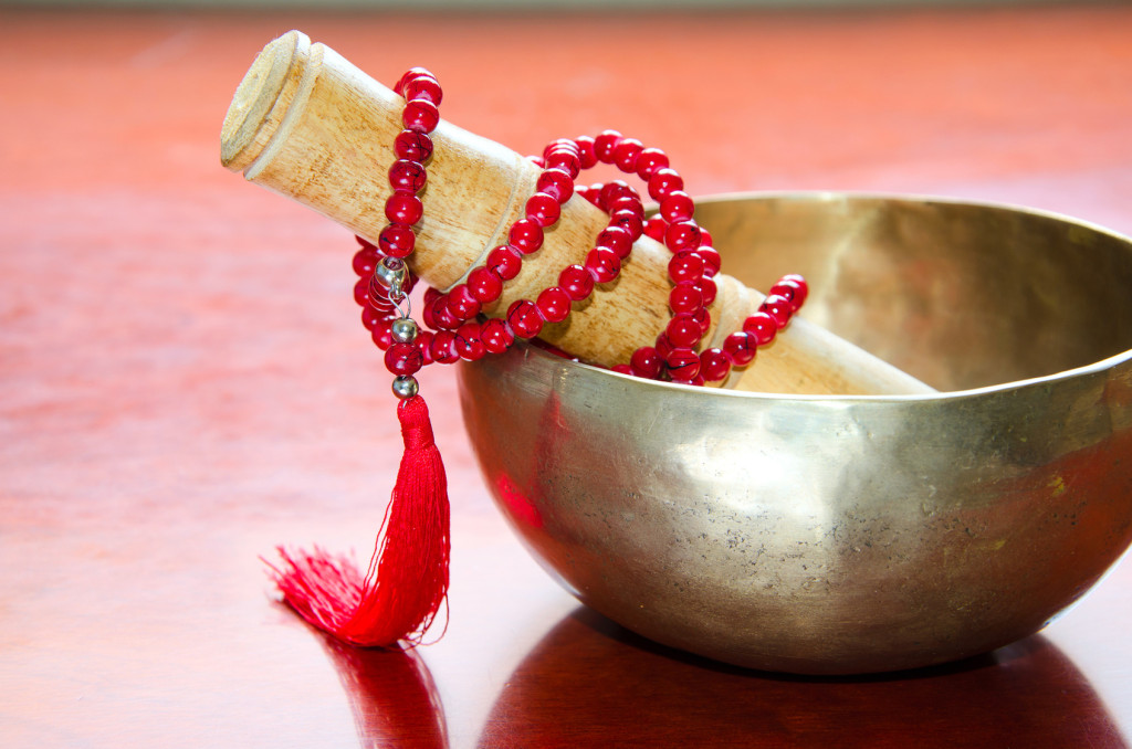 Closeup of a tibetan bowl and red  mala beads for meditation on wooden background.