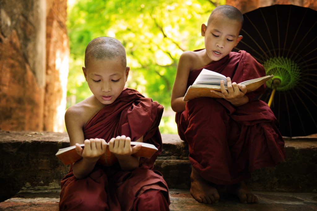 Southeast Asian Myanmar little monk reading book outside monastery, Buddhist teaching.