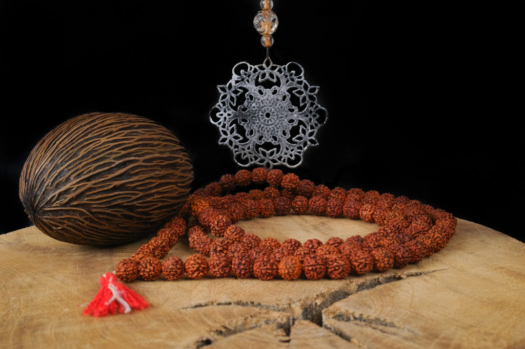 Indian art - tin mandala, prayer beards from Rudraksha, Foxtail palm seed on teak wood and black background